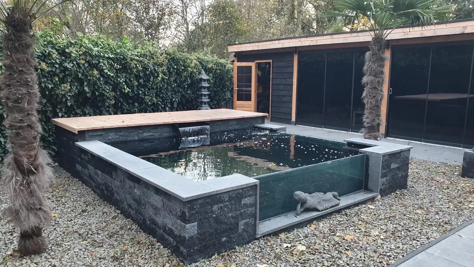 Opgebouwde vijver met stenen wanden, houten vlonder en waterval