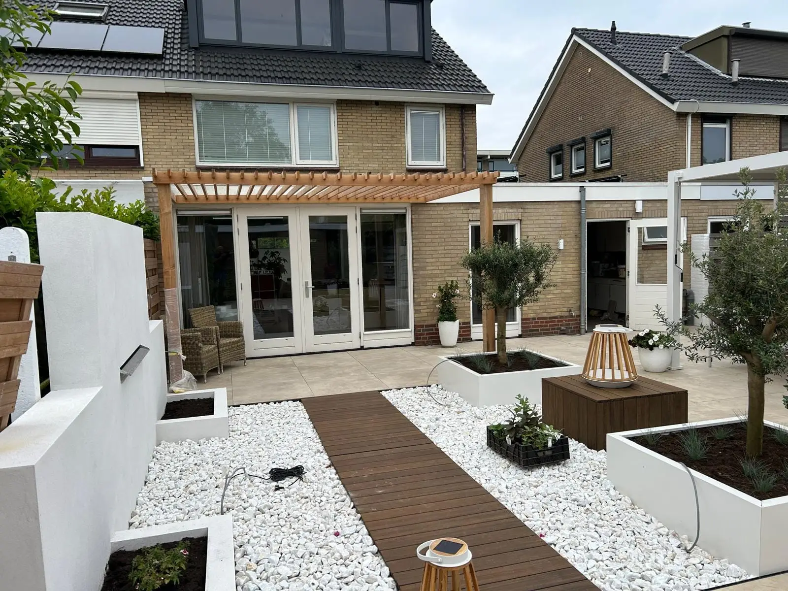 Strak aangelegde tuin met witte kiezels, een houten pad en plantenbakken