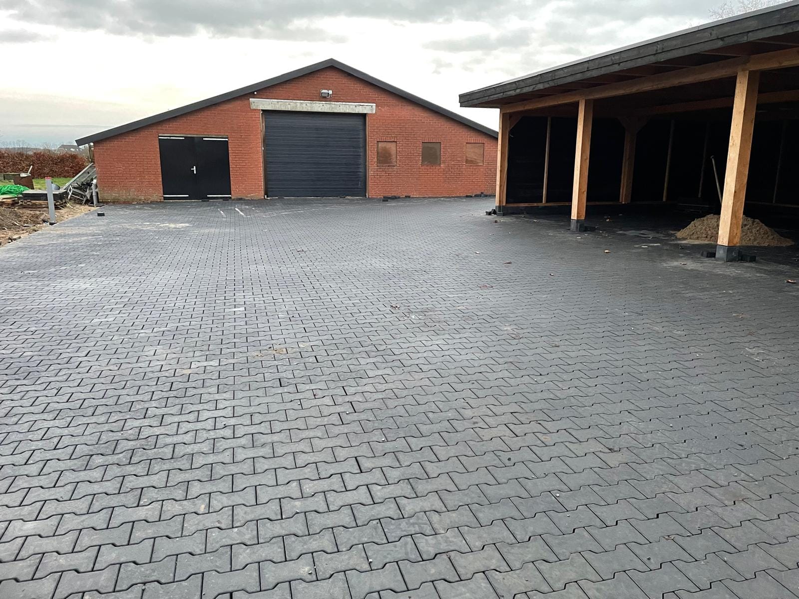 H-verbandstenen bestrating op een groot terrein bij een agrarisch bedrijf, inclusief bestrating onder een overkapping, uitgevoerd door De Tuynderie.