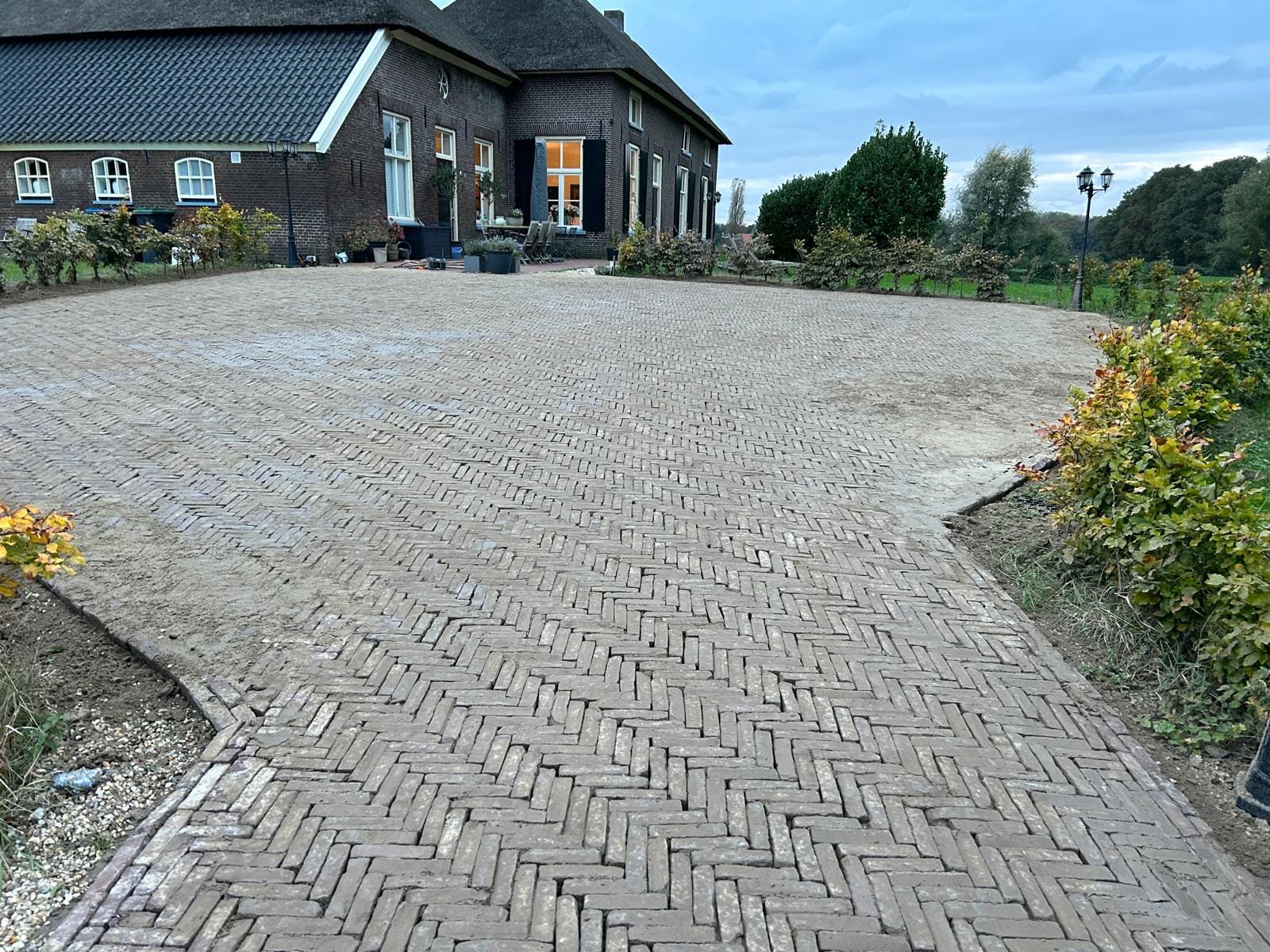 Klinkerbestrating aangelegd bij een karakteristieke woonboerderij, uitgevoerd door De Tuynderie.