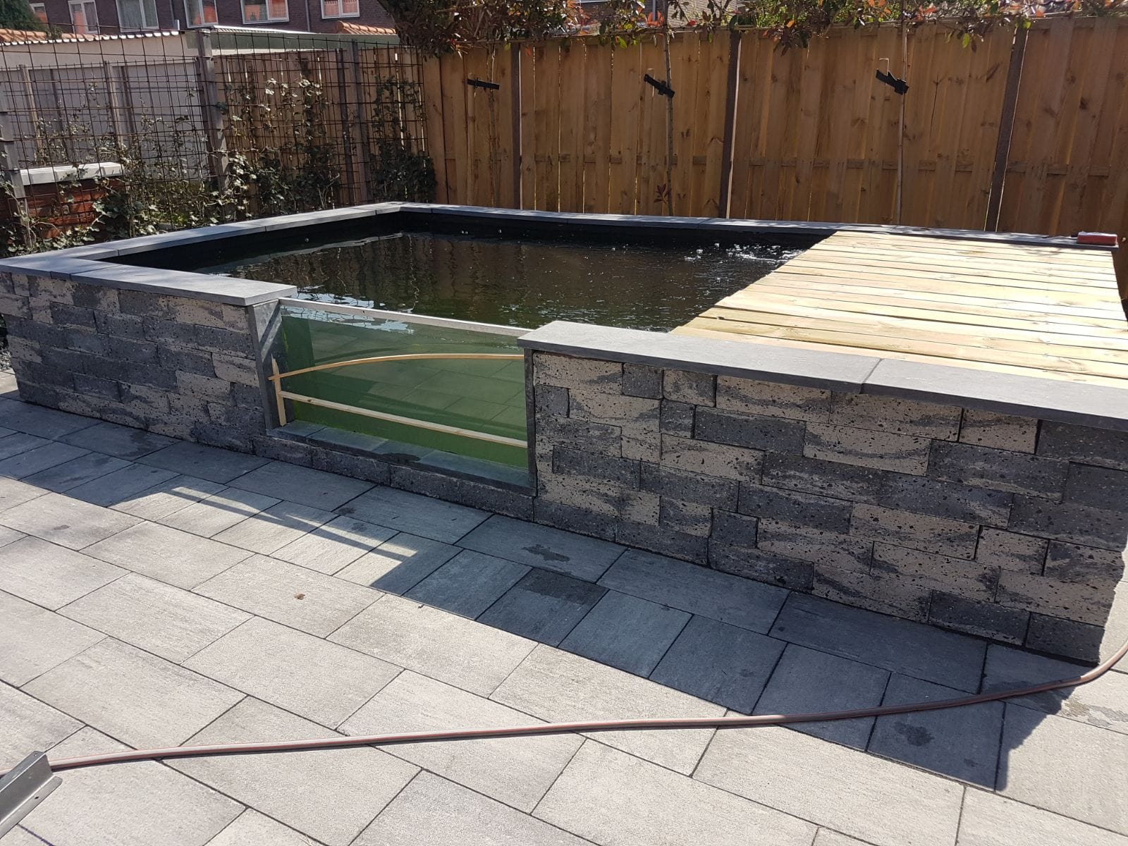 Opgebouwde vijver uit strakke stenen met houten vlonder, aangelegd door De Tuynderie.
