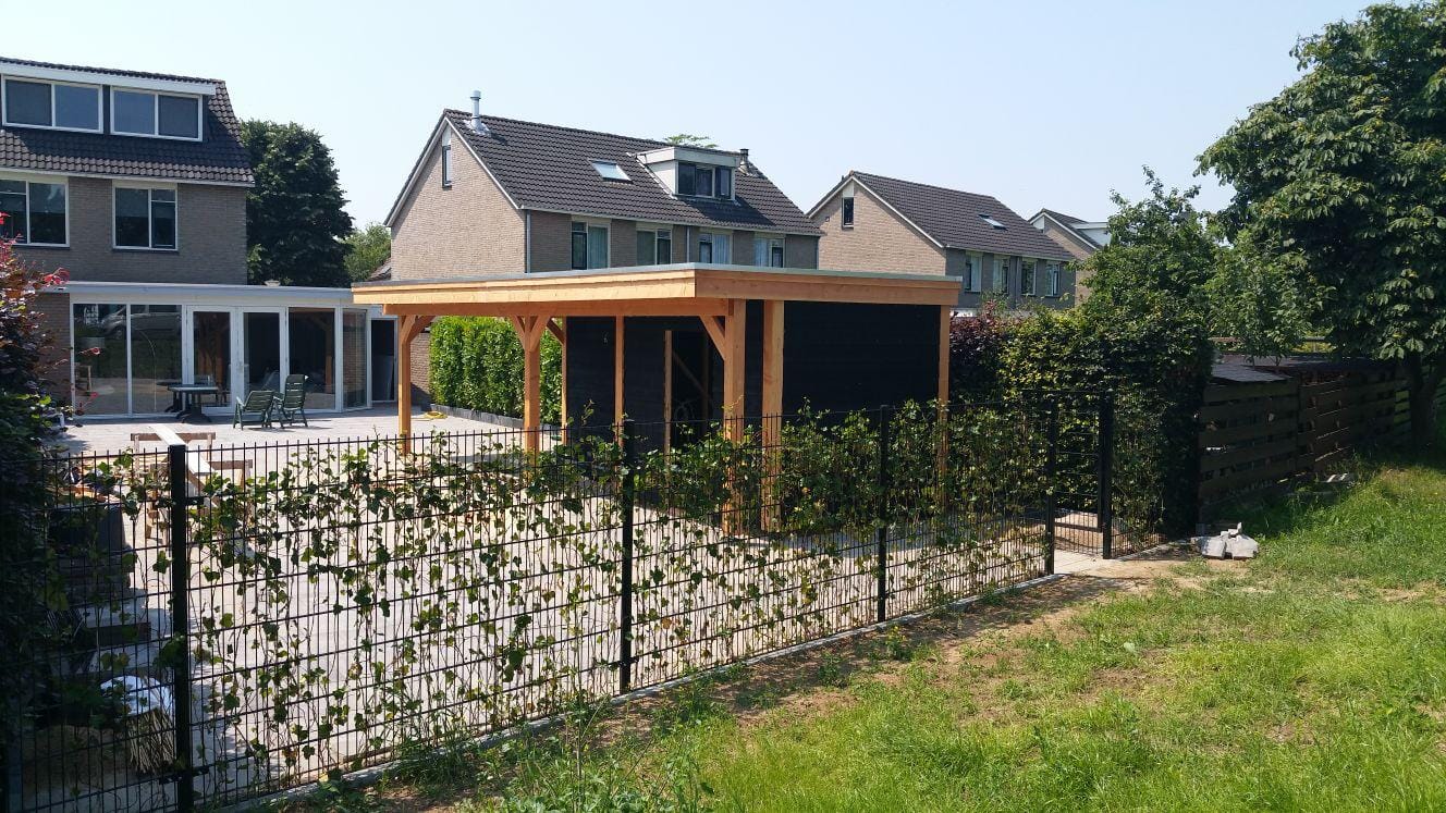 Tuin met overkapping, stalen hek omheining en een groene hedera klimop haag, aangelegd door De Tuynderie.